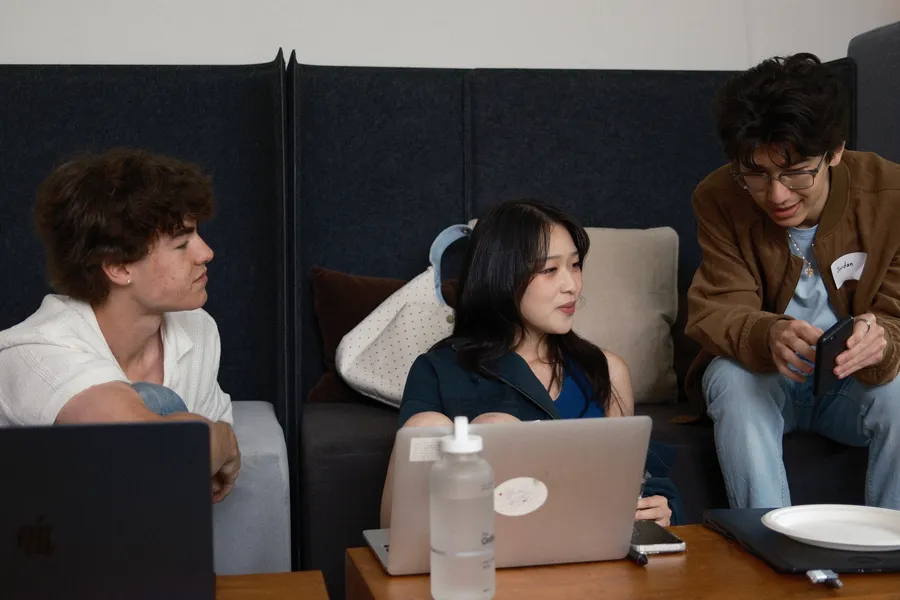 Three people on a couch with laptops open, mid-conversation.