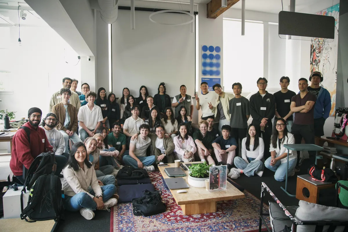 A big group photo of everyone at a Build Club session, sitting and standing around a rug.
