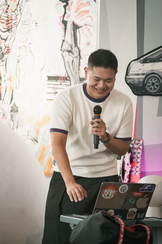 A builder laughing into a microphone while holding a laptop covered in stickers.