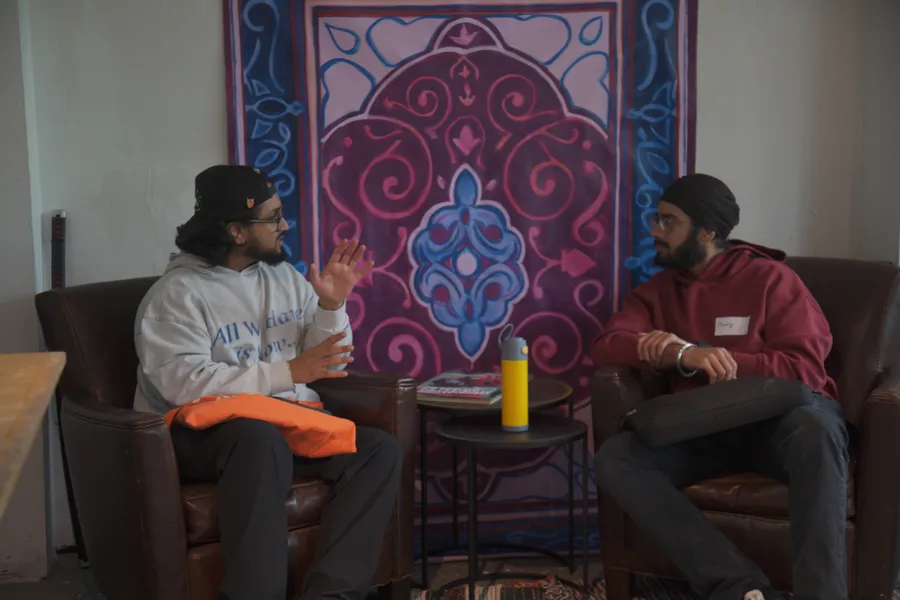 Two builders talking in leather armchairs under a Persian rug hung on the wall.