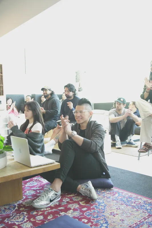 A builder sitting cross-legged on a Persian rug next to an open laptop, laughing with the people around them.