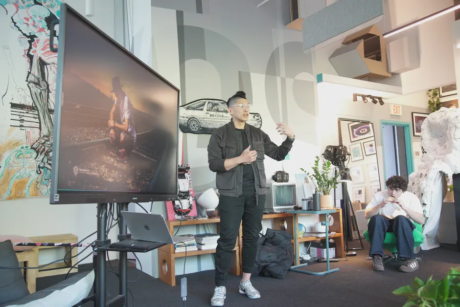 A guest presenting next to a large screen while people listen and work.